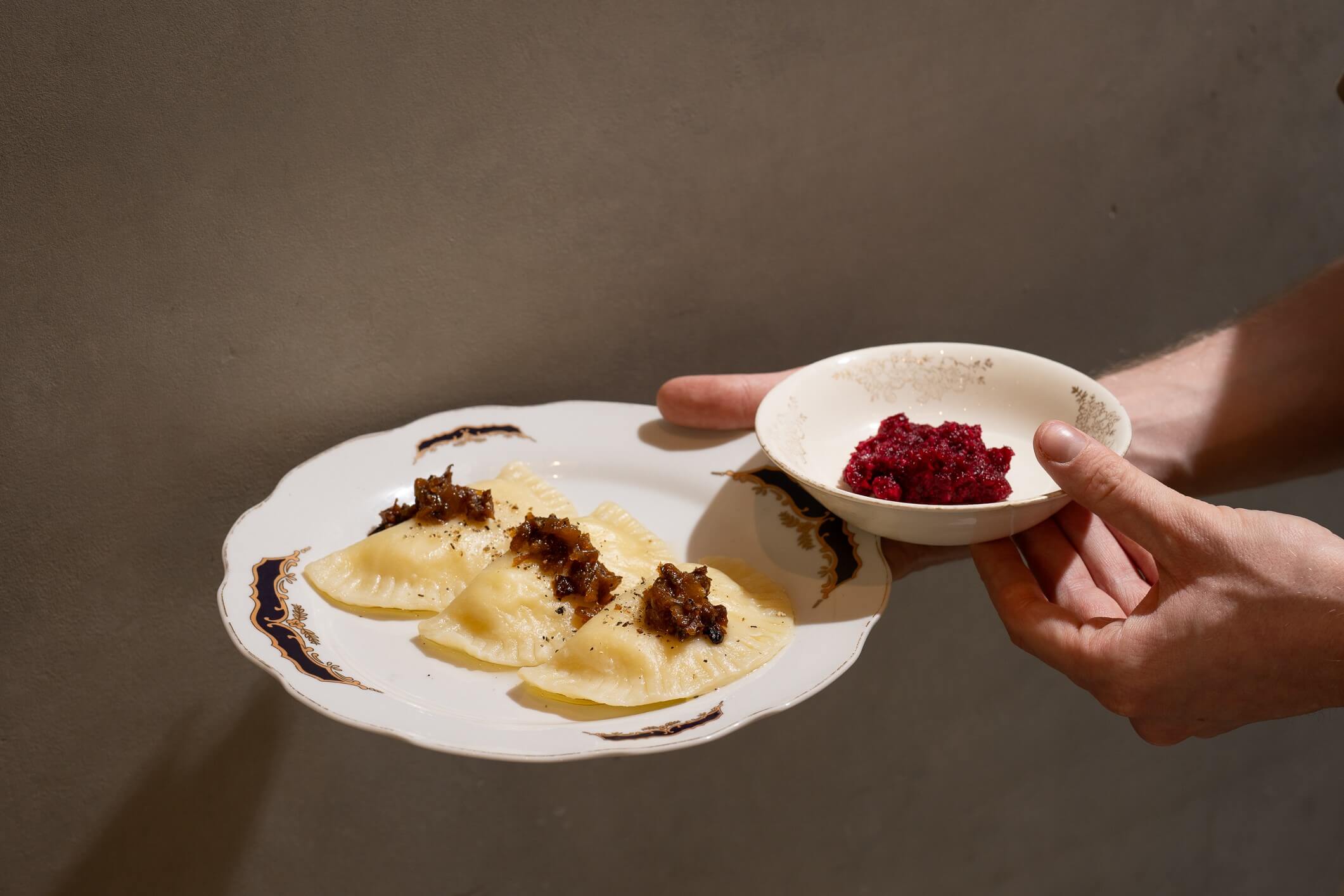 ידיים מחזיקות צלחת ורניקי עם בצל מטוגן וקערת חזרת ליד